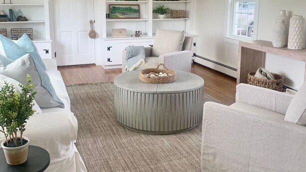 Een woonkamer met een ronde salontafel, witte banken en een boekenkast met decoratieve objecten.