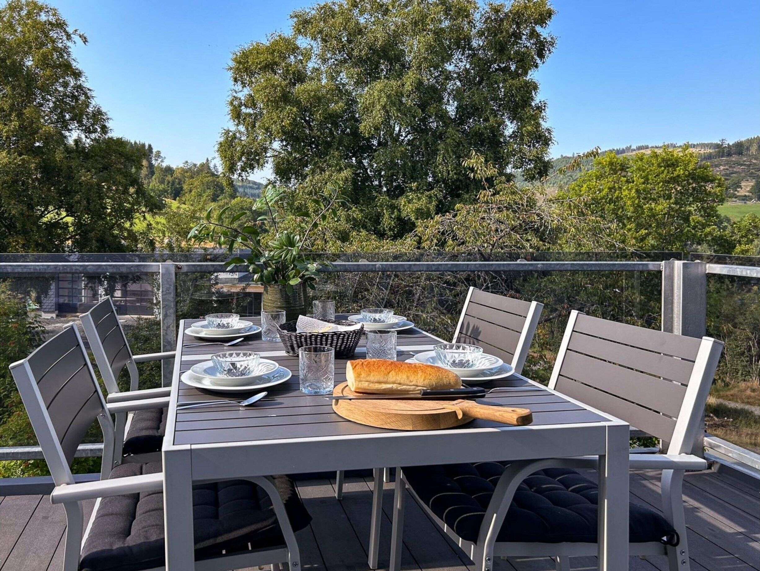 A deck with a table set for dining, surrounded by chairs, overlooking a scenic landscape.