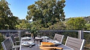 A deck with a table set for dining, surrounded by chairs, overlooking a scenic landscape.