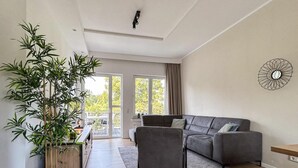 A modern living room with a grey sectional sofa, a large potted bamboo plant, and a view of the outdoors through large sliding glass doors.