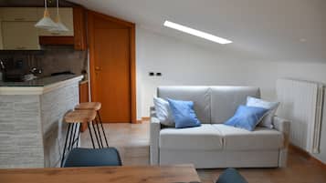 A modern kitchen with a built-in island, a dining area with a wooden table, and a living room with a sofa and cushions.