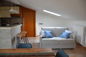 A modern kitchen with a built-in island, a dining area with a wooden table, and a living room with a sofa and cushions.