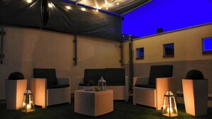Een overdekt terras met rieten meubels en lantaarns.