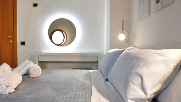 Een slaapkamer met een rond dakvenster, een bed met witte beddengoed en een nachtkastje met opgerolde handdoeken.