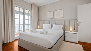 Un dormitorio moderno con una cama grande, lámparas de noche, vistas al mar y dos cuadros en la pared.