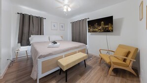 A bedroom with a bed, a bench, a chair, a ceiling fan, and a cityscape painting on the wall. - Spacious 4BEDR/2BATH Getaway w/ King Beds + TVs (Westworth Village)