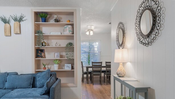 A living room with a blue sofa, a dining area with a table and chairs, a decorative mirror, and a bookshelf with various items. - Spacious 4BEDR/2BATH Getaway w/ King Beds + TVs (Westworth Village)
