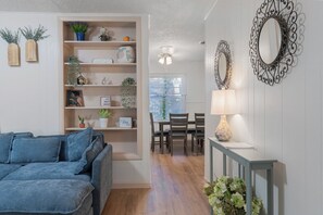 Un salon avec un canapé bleu, un coin repas avec une table et des chaises, un miroir décoratif et une bibliothèque contenant divers objets.
