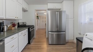A modern kitchen with white cabinetry, stainless steel appliances, and a wooden floor. - Spacious 4BEDR/2BATH Getaway w/ King Beds + TVs (Westworth Village)
