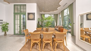 A dining area with a round table and wicker chairs, a green door, and large windows with curtains. - Luxury 4 bedroom Garden View Solar Villa - Tropical Garden Khem Beach (Phu Quoc)