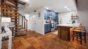 Une cuisine avec des meubles bleus, un plan de travail blanc et un escalier en bois.