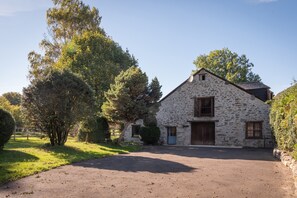 Un bâtiment en pierre avec une allée pavée et un grand arbre devant.
