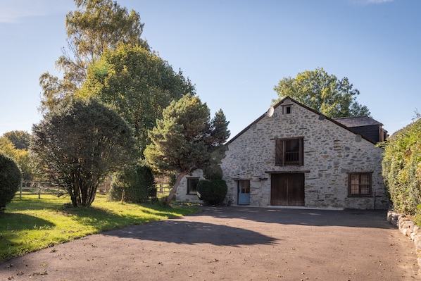A stone building with a paved driveway and a large tree in front.