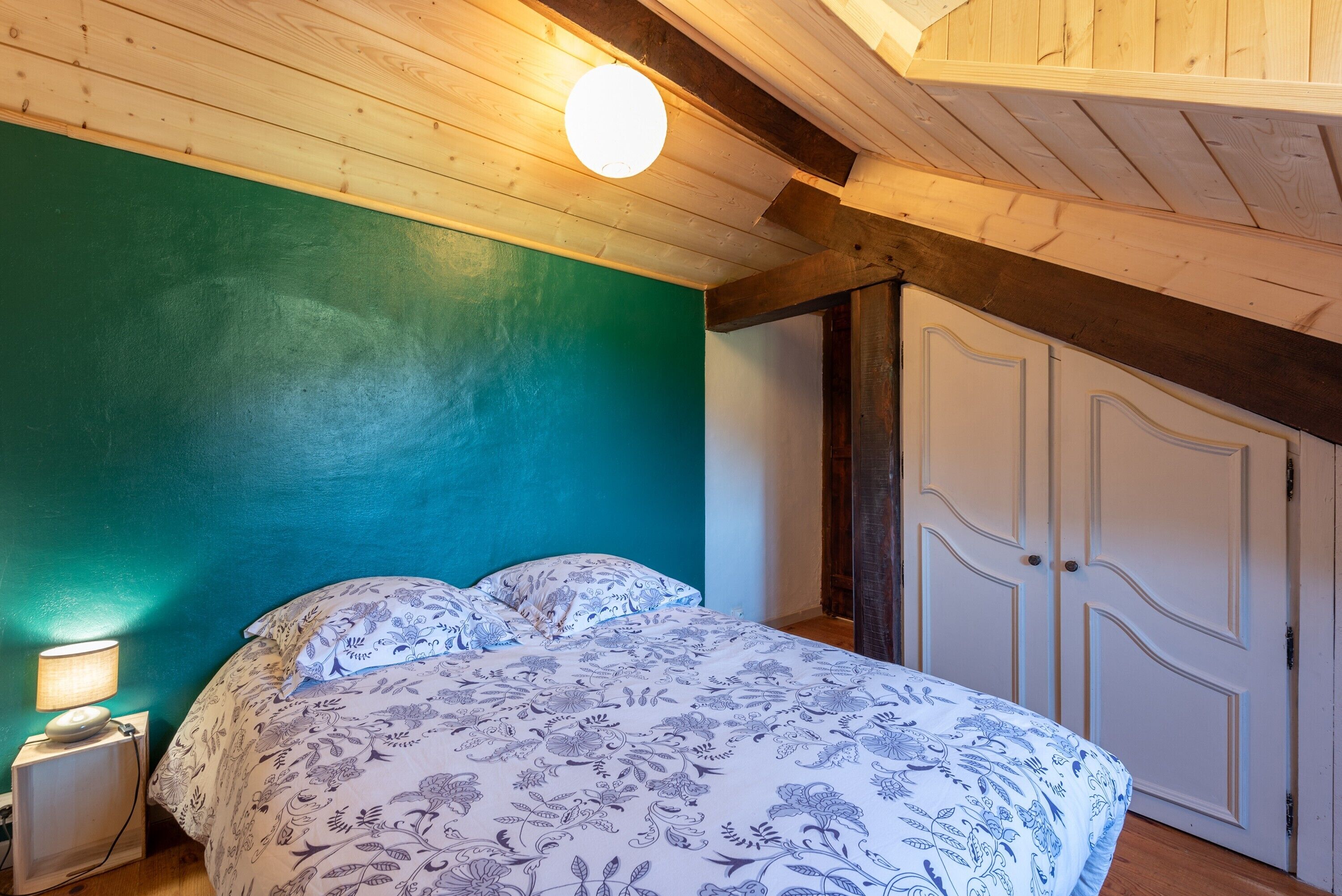 Une chambre à coucher avec un lit, une table de chevet, une lampe fixée au mur et une porte.