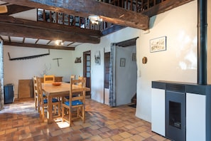 A rustic interior with a wooden dining table, chairs, a fireplace, and a staircase leading to an upper level.