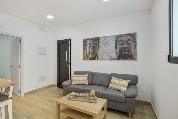 A modern living room with a grey sofa, wooden coffee table, and a Buddha statue.