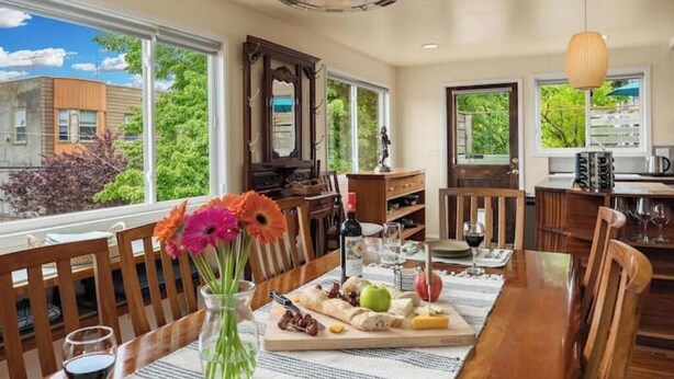 A dining area with a wooden table set for a meal, a vase with flowers, and a view of greenery outside. - QAnne Hideaway•PrivateDeck•Jacuzzi Tub•CA King•BBQ (Seattle)