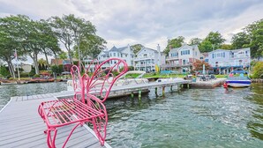 Un quai avec une chaise rose, un bateau et des maisons en arrière-plan.