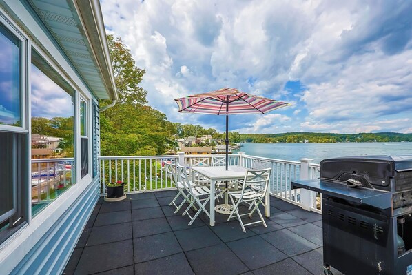 A balcony with a table and chairs, a grill, and a view of a lake.
