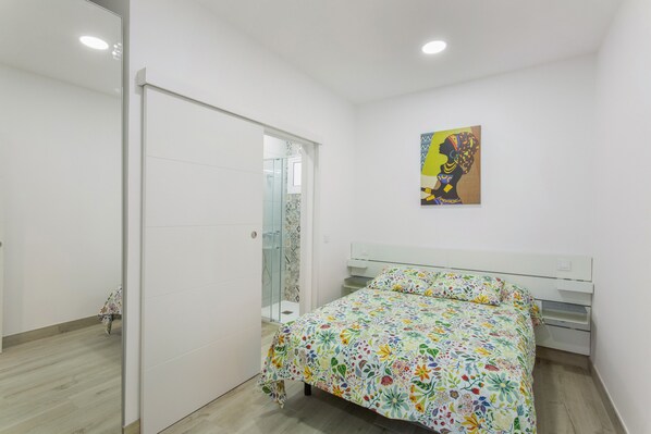 Un dormitorio con cama, un armario blanco, cabina de ducha de vidrio y un cuadro en la pared.