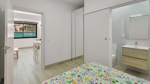 Een slaapkamer met een bed, een badkamer met een wastafel, en uitzicht op een straat.