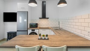 Een moderne keuken met een houten tafel, witte stoelen, een zwarte kookplaat, een magnetron en een wasmachine.