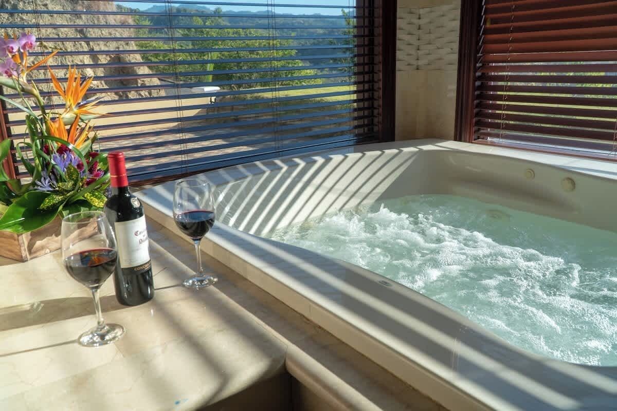 Un bain à remous rempli d’eau, une bouteille de vin et deux verres à vin, le tout posé sur une surface en marbre.