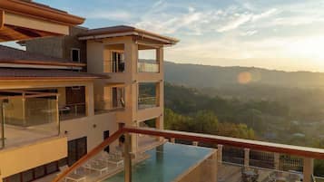 Un immeuble à plusieurs étages doté d’une piscine à débordement sur le toit, d’un balcon et offrant une vue sur un paysage vallonné.