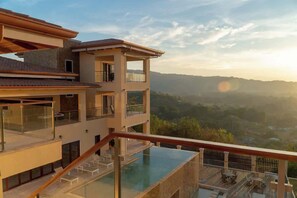 Un immeuble à plusieurs étages doté d’une piscine à débordement sur le toit, d’un balcon et offrant une vue sur un paysage vallonné.