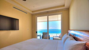 A bedroom with a large bed, a television mounted on the wall, and a sliding glass door leading to a balcony with a view of the ocean. - Direct Beach Front Ocean View on 7th Floor (Jacó)
