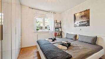 A bedroom with a bed, a window, a radiator, a bookshelf, and a wall-mounted picture.
