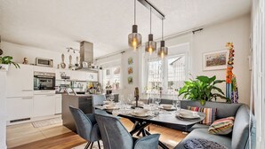 A modern kitchen with white cabinets, a dining area with a table set for four, and a gray sofa with colorful cushions. - Retreat Living • Sauna - Garden - Parking lot (Bensheim)