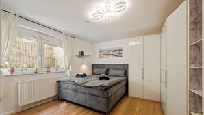 Ein modernes Schlafzimmer mit grauem Bett, weißem Kleiderschrank und einem Fenster mit Vorhängen.