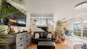 Ein modernes Wohnzimmer mit einer schwarzen Ledersofa, einem weißen Ottomanen und einem Weihnachtsbaum.
