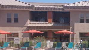 A swimming pool with lounge chairs and umbrellas, a warning sign, and a building with a balcony.