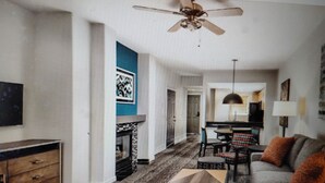 A living room with a sofa, coffee table, and fireplace. There is a ceiling fan and a TV mounted on the wall.