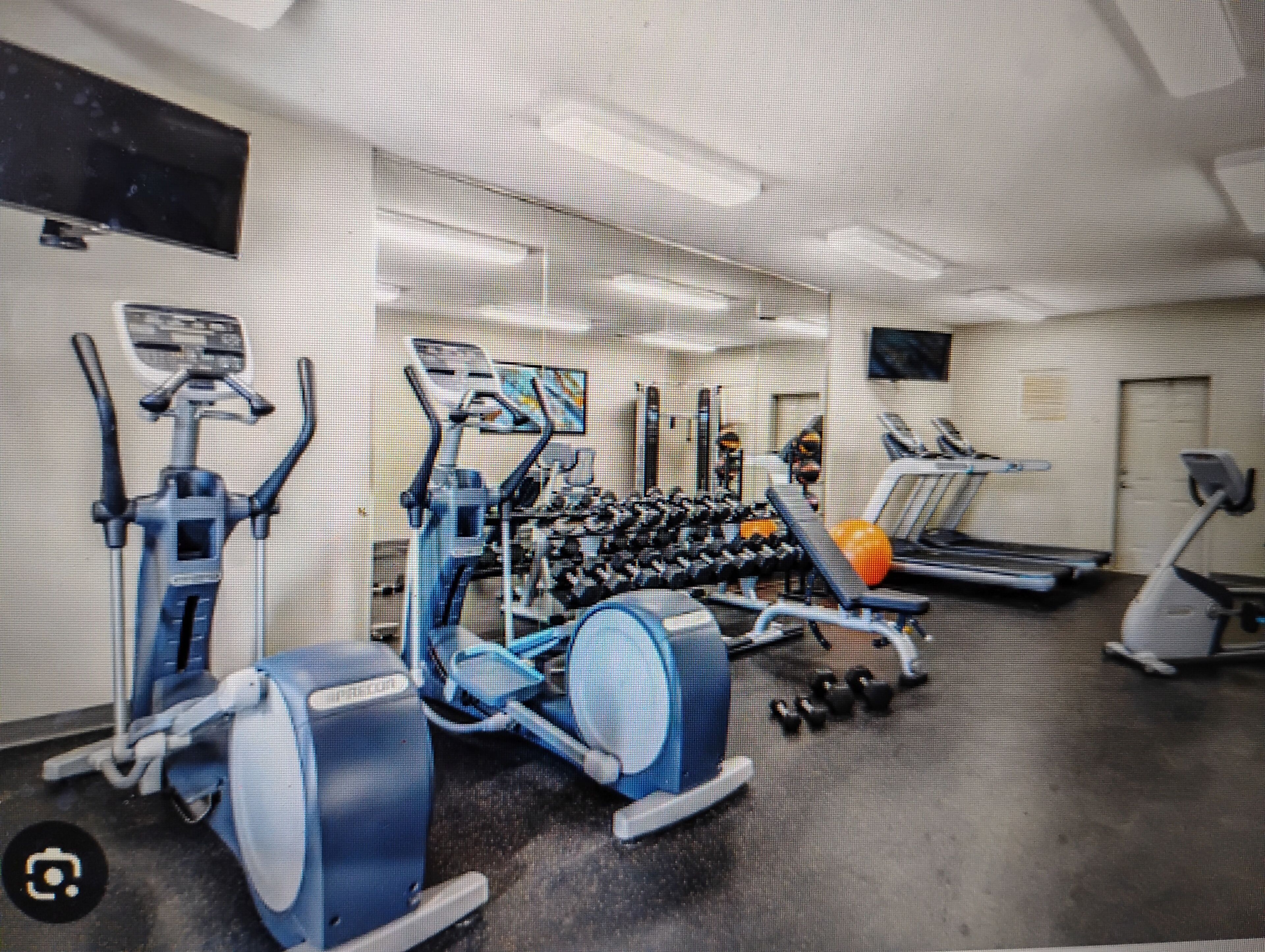 Une salle de sport équipée de divers appareils, notamment un tapis de course, un vélo elliptique et des appareils de musculation.