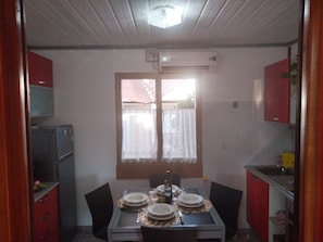 A compact kitchen with a dining table set for four, a refrigerator, and a window with curtains.