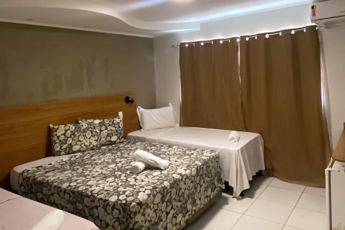A hotel room with two beds, a wooden headboard, a small table, and a curtain.