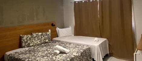 A hotel room with two beds, a wooden headboard, a small table, and a curtain.