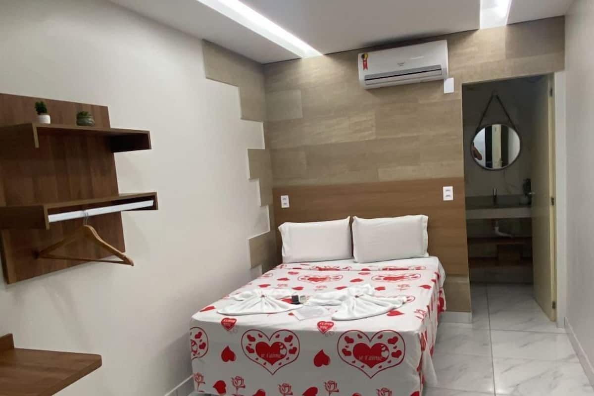 A modern hotel room with a bed, bedside tables, a built-in shelf, and a bathroom visible through an open door.