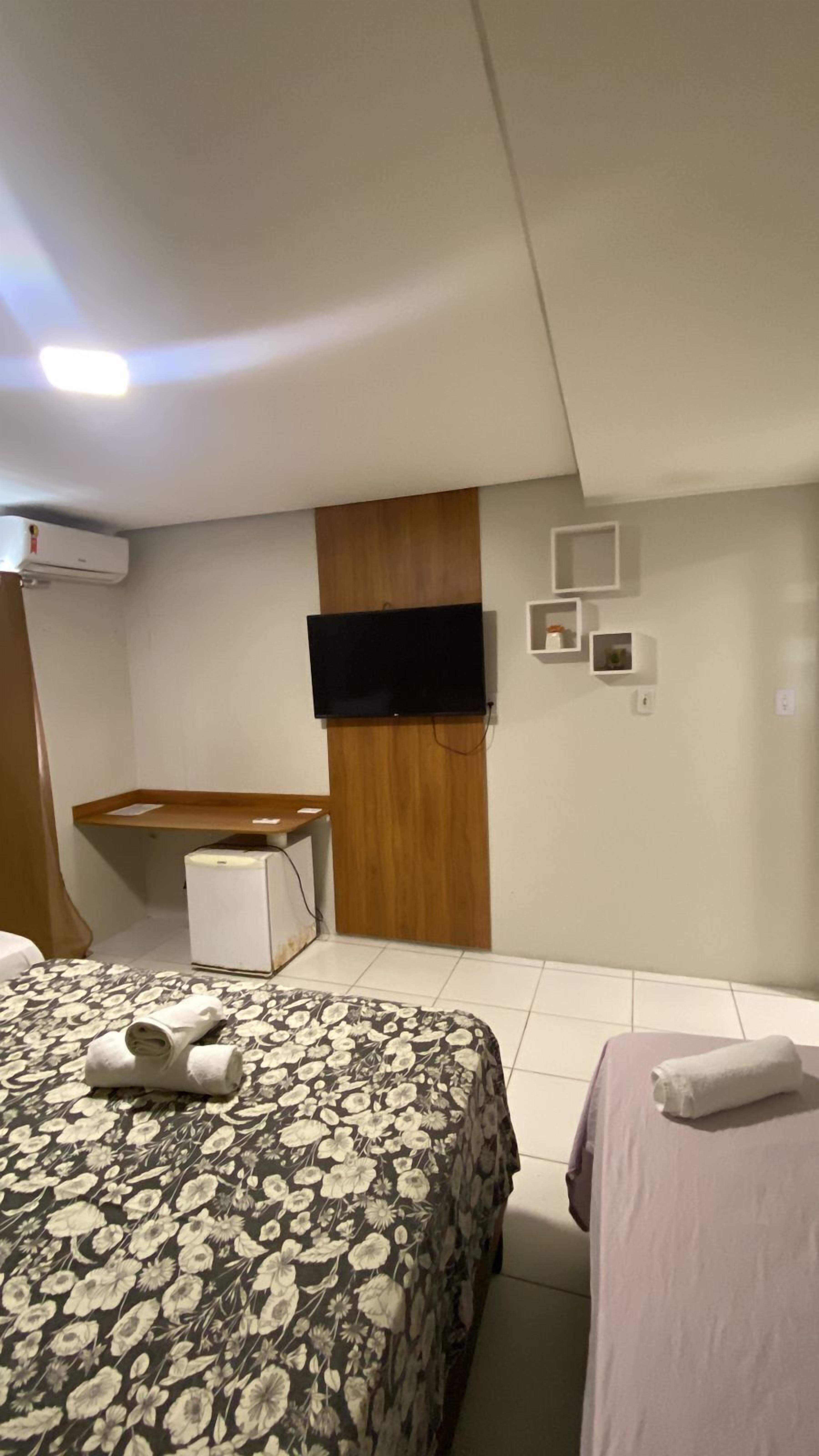 A hotel room with a bed, a desk, a flat-screen TV, and a wall-mounted air conditioner.