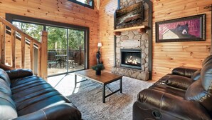 A cozy cabin interior with a stone fireplace, leather sofas, and a dining area with a view of the outdoors.