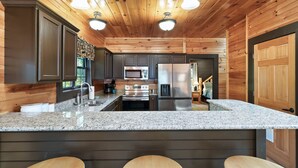 A modern kitchen with granite countertops, stainless steel appliances, and wooden paneling.