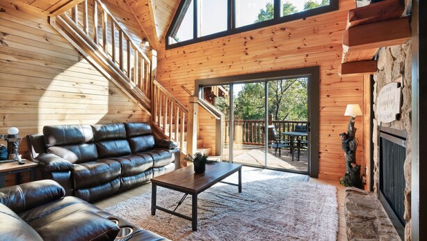 A spacious living area with a wooden staircase, leather sofa, and a large window offering a view of the outdoors.