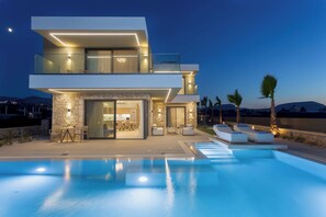 A modern two-story house with a swimming pool, outdoor seating, and a stone facade. - Divel Luxury Villas - Villa Inder with Heated Pool, by Estia (Agkisaras)