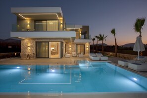 Una moderna casa a due piani con piscina, area relax esterna e facciata in pietra.
