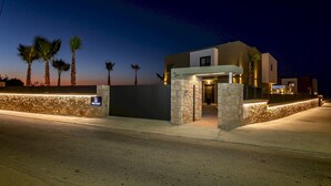 Un edificio moderno con fachada de piedra, una entrada bien iluminada y palmeras al fondo.