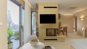 A modern living room with a fireplace, a flat-screen TV mounted on the wall, and a dining area with a bowl of snacks.