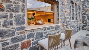 A stone exterior wall with a window, two wicker chairs, and a small table with a plant.